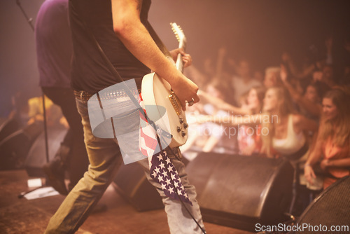 Image of Music festival, performer and playing guitar for entertainment, night and artist with musical instrument. Back, person and american flag for patriotism at concert, audience and crowd on usa stage