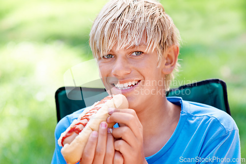 Image of Child, eating and portrait with hotdog outdoor in camping chair and relax at barbecue with lunch. Happy, kid and hungry for food from bbq in park, woods or forest on holiday or vacation in summer