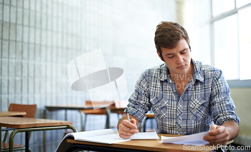 Image of Student, reading and learning in classroom for education, language development or knowledge in university. Young man writing notes and books for college research, essay paper or course information