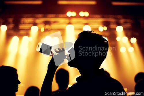 Image of Night, club and man with a drink at party, event or music festival with stage lights and silhouette. Dark, concert and person dance with bottle of alcohol in crowd at social celebration or rave