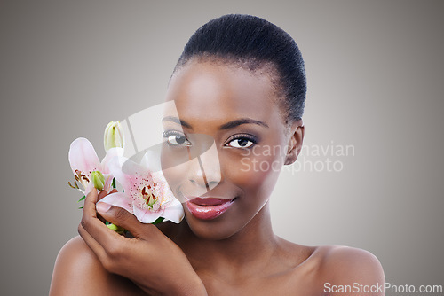 Image of Portrait, beauty and flower with natural black woman in studio on gray background for wellness. Face, skincare and orchid with confident young person at spa or salon for aesthetic dermatology