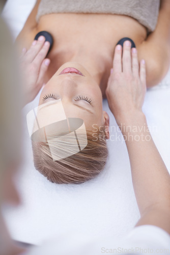 Image of Woman, hands and massage with hot stone on bed, health resort and body treatment for wellness or zen. Person, heat or masseuse for sleep for peace, above or muscle comfort with detox at spa clinic