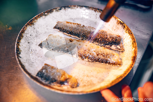 Image of Chef cooks fish using gas burner torch.