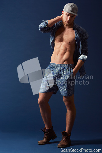 Image of Fashion, portrait or model with six pack in studio on a blue background in an open unbuttoned shirt. Body, chest or handsome male person posing on color wall for masculine style with a trendy cap