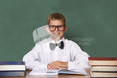 Image of Boy child, books and school in portrait with smile, information and knowledge with pride in classroom. Student kid, happy and excited for education, learning and development by chalkboard at desk