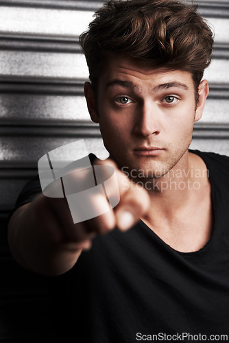 Image of Fashion, serious and portrait of man with pointing gesture for calling, direction or scolding. Angry, finger and handsome young male person with casual, trendy or cool style by steel garage door.