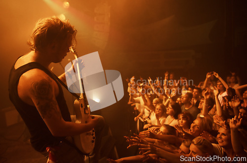 Image of Guitar, concert and crowd at stage with man in performance of rock, metal and music. Festival, event and audience of people in celebration of talent in theater at night with spotlight and energy