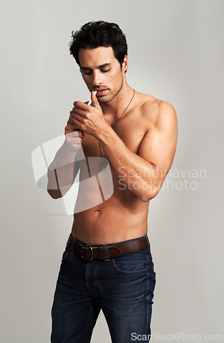 Image of Shirtless, cigarette and man smoking in a studio for grungy, cool and attractive personality. Confidence, smoke and young male model from Canada with tobacco in jeans isolated by gray background.