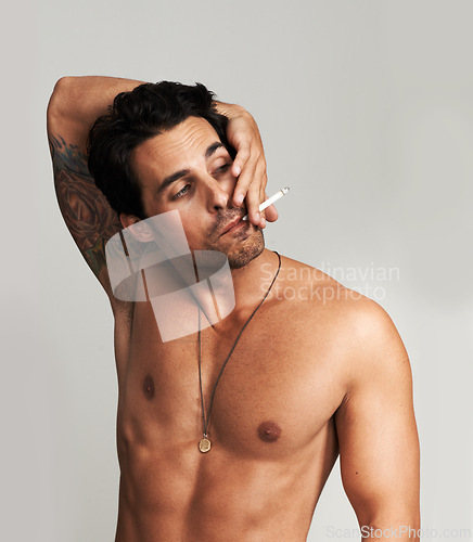 Image of Shirtless, cigarette and man smoking in a studio for grungy, cool and attractive personality. Confidence, chest and young male model from Canada with tobacco for smoke isolated by gray background.