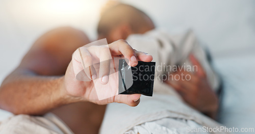 Image of Hand, condom and people in bed for sex, protection and contraception with lust and desire on Valentines day. Intimacy, health and safety for couple bonding in bedroom with rubber and sexual moment