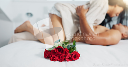 Image of Couple, red roses and lying on bed for anniversary, love or valentines day in romance, embrace or trust at home. Romantic man and woman in bedroom intimacy, passion or bonding with flowers at house