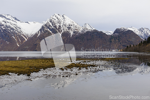 Image of Overlooking the calm sea with snow-capped mountains in the backdrop at dusk.