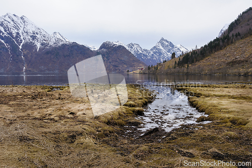 Image of Alpine scenery with a tranquil fjord, snow-dusted mountains, and early spring foliage.