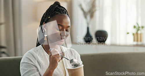 Image of Black woman on sofa, eating ice cream and relax in living room with smile, summer pleasure and enjoy. Happiness, fun or thinking, girl on couch with taste of frozen chocolate getalo dessert in home.