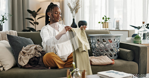 Image of Laundry, housework and a black woman folding washing on a sofa in the living room of her home to tidy. Smile, relax and a happy young housewife cleaning her apartment for housekeeping or hygiene