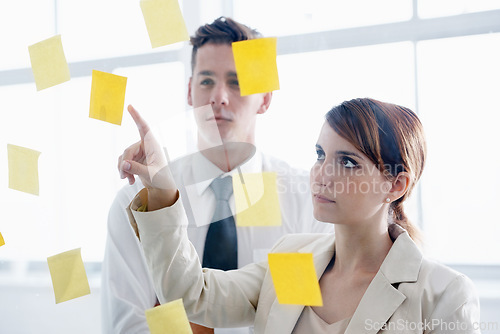 Image of Teamwork, brainstorming and meeting in office with sticky notes for planning, ideas and schedule. Colleagues, thinking and pointing at paper for collaboration, vision and strategy on glass wall