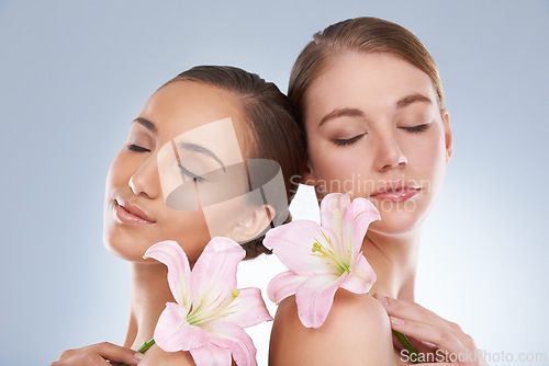 Image of Woman, relax and skincare with flowers for natural beauty, makeup or cosmetics on a blue studio background. Young female, people or models smile in satisfaction for spa, soft skin or facial treatment