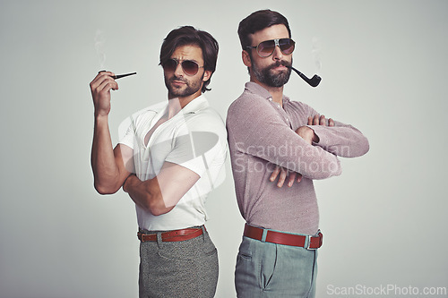 Image of Fashion, men and sunglasses or pipe in studio with vintage model, hipster outfit and confidence with arms crossed. Friends, people and attitude with 70s style or retro clothes with white background