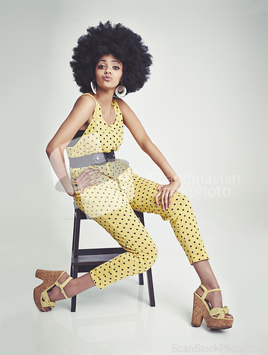 Image of Black woman, portrait and relax on chair in fashion, yellow jumpsuit or high heels on a gray studio background. African female person with afro, makeup or jewelry in beauty or style on mockup space