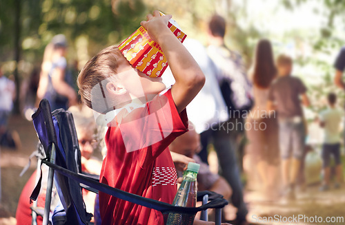 Image of Festival, party and boy eating popcorn outdoor in summer at event for celebration or entertainment. Kids, food or snack and young child eating from box in nature, forest or woods alone with chair