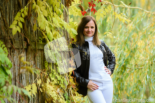 Image of A young beautiful girl pressed her back against a wooden wall against the background of an autumn forest and looks into the frame