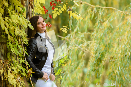Image of A young beautiful girl pressed her back against a wooden wall and looks at the autumn forest