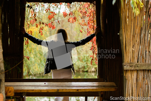 Image of Young beautiful girl standing in the doorway of an old hut, rear view