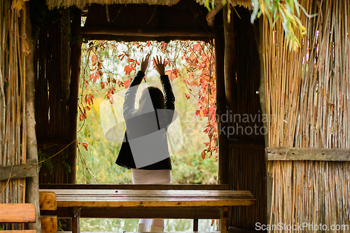 Image of A young beautiful girl stands in the doorway of an old hut and raised her hands up