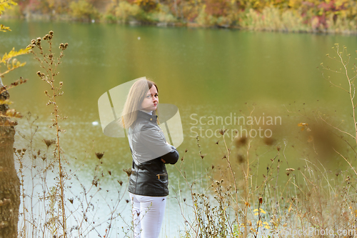 Image of A girl stands by the lake on a warm autumn day, turned around and looked into the frame