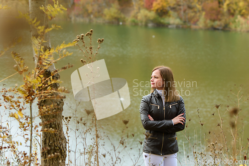 Image of A girl stands by the lake on a warm autumn day and looks thoughtfully into the distance.