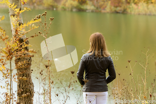 Image of A girl stands by the lake on a warm autumn day, view from the back