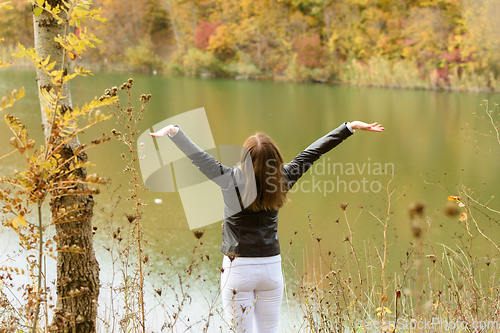 Image of The girl by the autumn lake joyfully raised her hands up