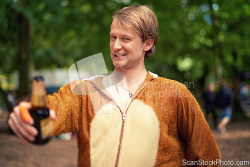 Image of Halloween, costume and man with beer to drink, toast and happy celebration outdoor in bear outfit. Animal, suit and person smile in portrait with lager, bottle and drunk from drinking alcohol in park