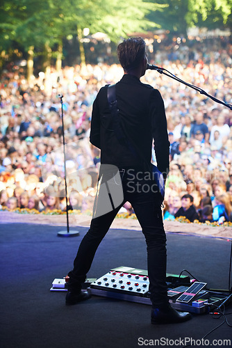 Image of Singer, music festival and man with performance, back and outdoor for event and crowd with celebration. Person, party and artist with microphone and audience with sunshine and fans screaming with fun