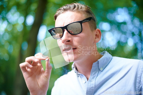 Image of Sunglasses, man and smoking weed outdoor at event, celebration and music festival alone. Cigarette, marijuana and face of young person at party, carnival and concert in nature with cannabis joint