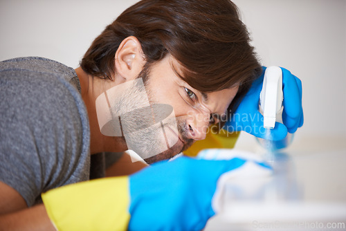 Image of Man, face and spraying surface for housekeeping, hygiene or disinfection on furniture or table at home. Male person, maid or cleaner checking dirty spots for wiping, bacteria or germ removal at house