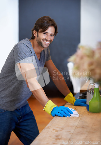 Image of Happy man, portrait and cleaning table for housekeeping, hygiene or disinfection on furniture or surface at home. Male person, maid or cleaner and gloves for wiping, bacteria or germ removal at house