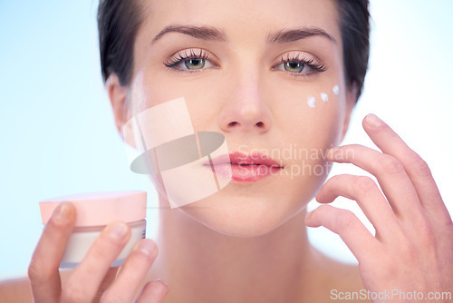 Image of Portrait of woman, application or face cream for skincare, beauty or cosmetics on blue background. Antiaging, studio or model with product, creme or glow for lotion, dermatology or facial treatment