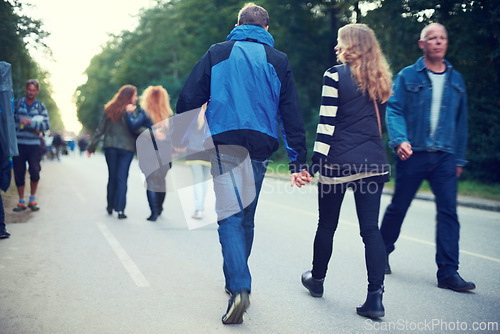 Image of Couple, back and holding hands while walking among trees and crowds along road in New Zealand. Rear view of man, woman and people for travel, date and bonding in busy woods, park and highway