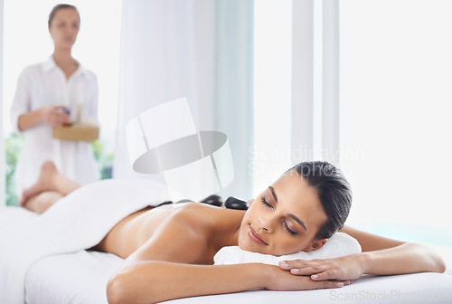 Image of Hot stone, massage and woman at spa to relax, beauty and pamper back for wellness at luxury salon. Therapist, rocks and person in treatment for skincare, peace or calm for healthy body with masseuse