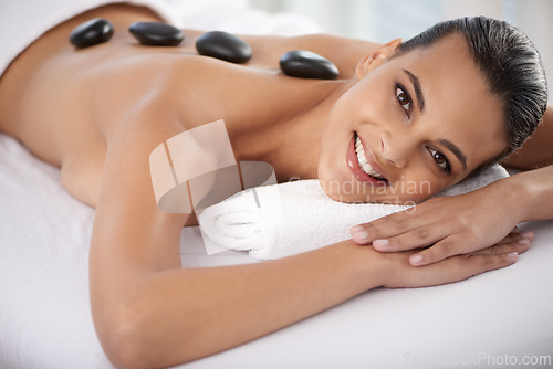 Image of Relax, hot stone and portrait of woman with massage at spa for wellness, health and back treatment. Self care, smile and young female person with cosmetic warm stone back therapy at beauty salon.