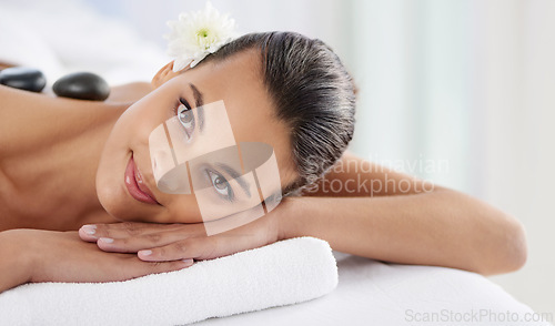 Image of Portrait, hot stone and woman laying for massage at spa for wellness, health and back treatment. Self care, cosmetic and young female person relaxing for warm rock therapy at natural beauty salon.