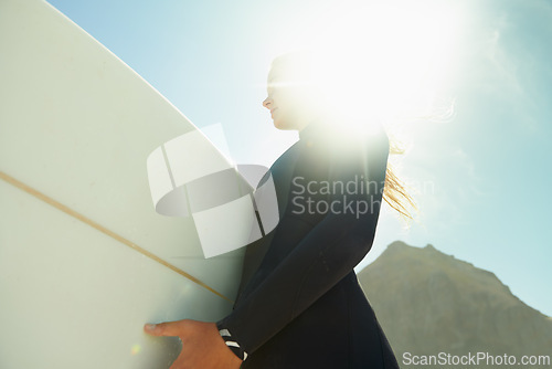 Image of Flare, sky at beach and woman with surfboard in summer from below for travel, vacation or holiday. Exercise, fitness or sports with confident young surfer person in wetsuit for leisure closeup