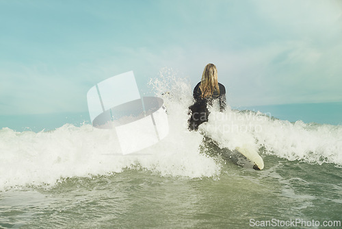 Image of Ocean, wave and splash with surfer woman in wetsuit for sports, fitness or exercise in summer from back. Blue sky, sea and surfing with person on surfboard in water for travel, vacation or holiday