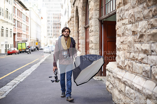 Image of Camera, equipment and photographer in city for photoshoot with lighting gear on street. Cameraman, walking and professional photography tools for press, project and person travel with technology