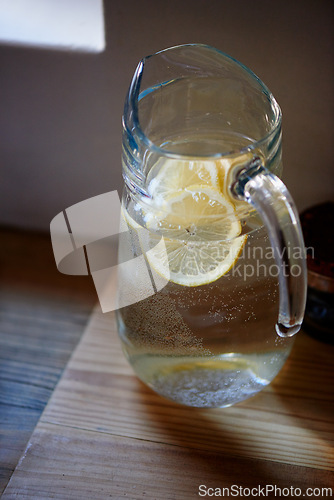 Image of Water, lemon and jug in kitchen for health benefits or detox drink for hydration or natural vitamins, organic or counter. Beverage, fruit and glass in home for antioxidants, vitamin c or immunity