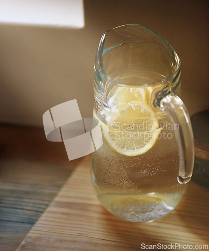 Image of Water, lemon and jug in kitchen for wellness or detox drink for hydration or natural vitamins, organic or counter. Beverage, sunshine and glass in home for healthy antioxidants, vitamin c or immunity