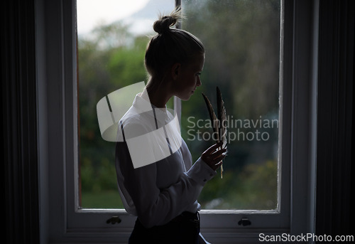 Image of Woman, feather and window in home for writing in dark room and mysterious aesthetic for artistic pose. Female writer, dim light and ink pen with thinking, author and old school setting for creativity