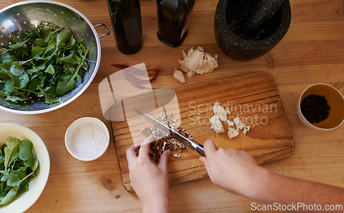 Image of Hands, chopping and ingredients in kitchen for salad preparation or walnuts, leafy greens or garlic. Person, knife and cooking vegan meal on wooden board with spices for nutrition, health or top view