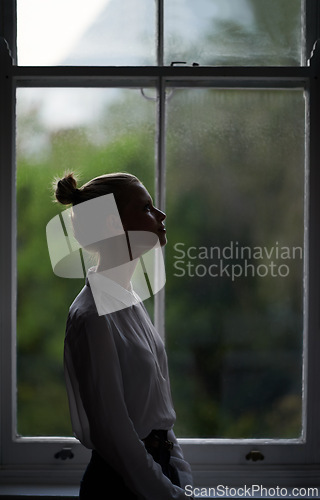 Image of Woman, window and thinking in home or dark in evening with anxiety or mental health, depression or thoughts. Female person, apartment and environment view or upset wondering for sad, grief or London